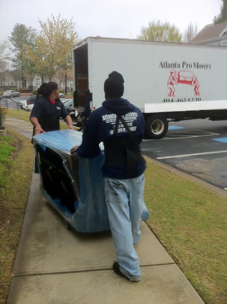 Two Atlanta Pro Movers subcontractors carefully transporting wrapped furniture to a moving truck in a residential area.