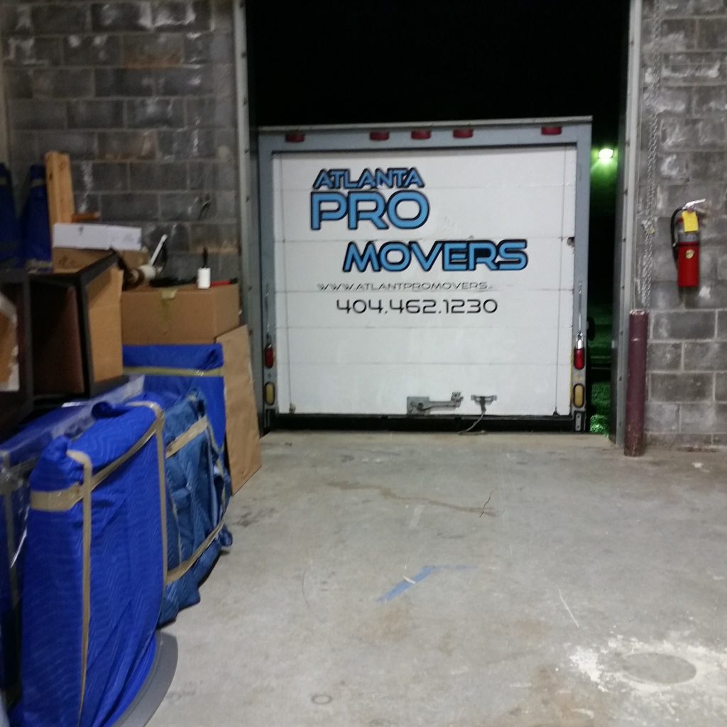 "Atlanta Pro Movers truck at warehouse loading dock with furniture and boxes secured under blue moving blankets – professional local and long-distance moving services."